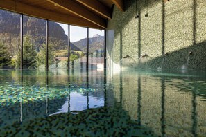 A large indoor swimming pool with a view of mountains through large windows. - Hotel Cailler (Charmey)