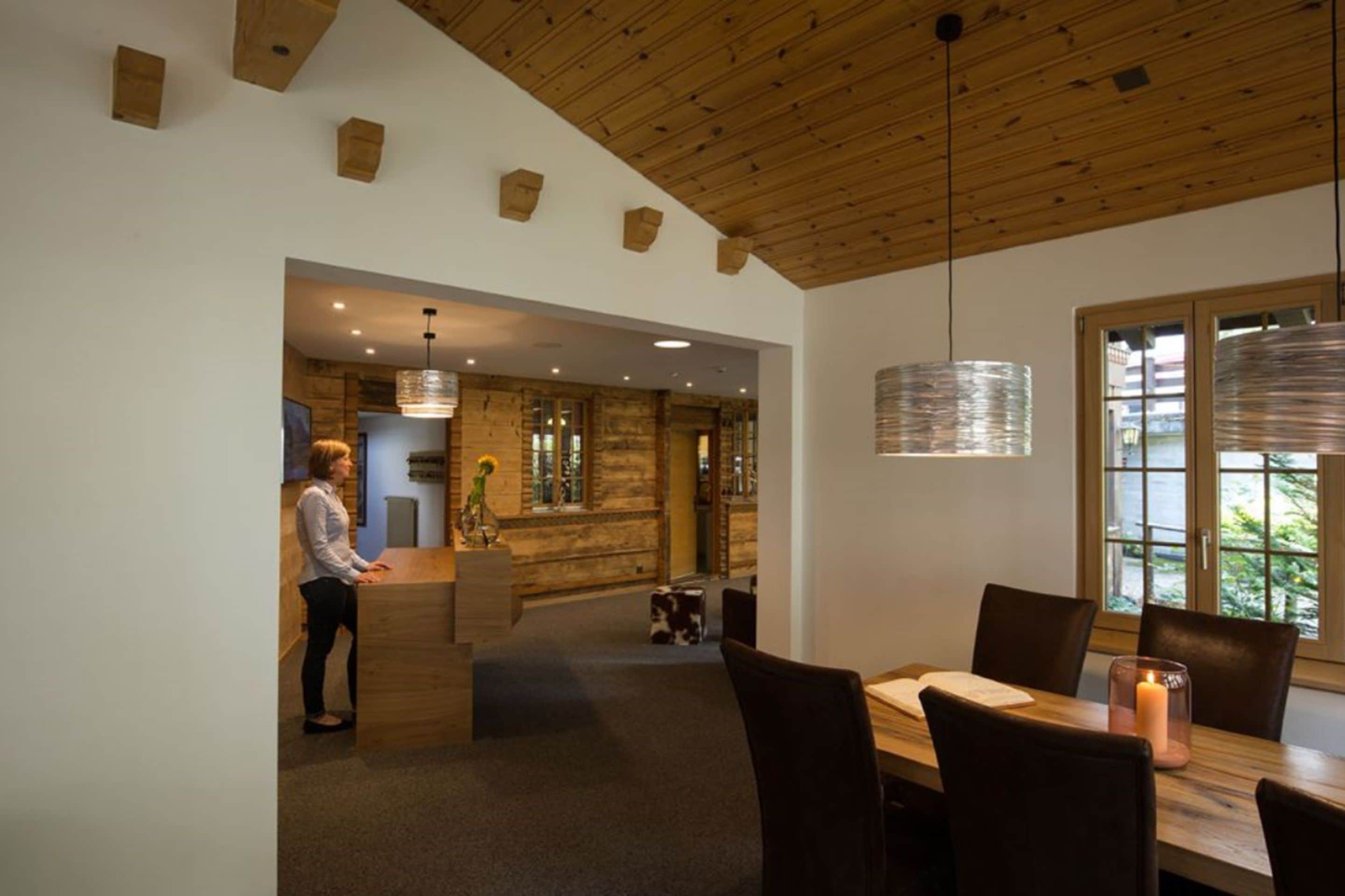 Moderne interiør med træloft, en receptionsdisk, et spiseområde med et lys og udsigt gennem et vindue.