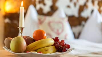 Un plato de fruta con manzanas, plátanos, uvas y una naranja, con una vela encendida al fondo.