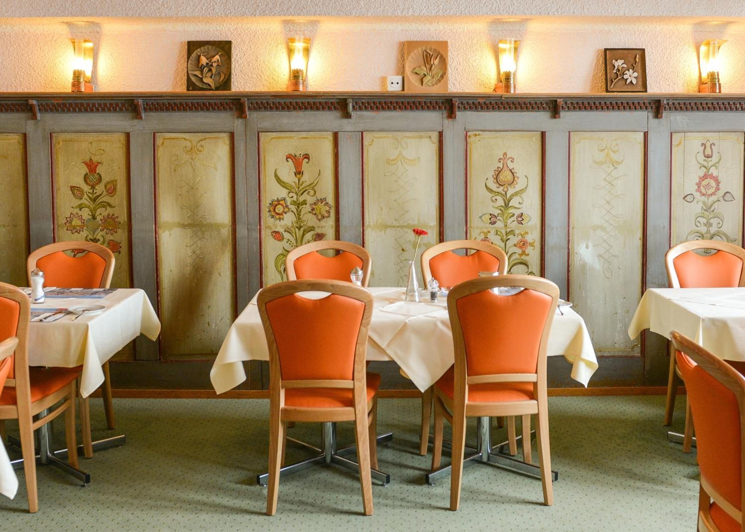 Un restaurant avec des tables et des chaises orange, dont les murs sont décorés de motifs floraux.