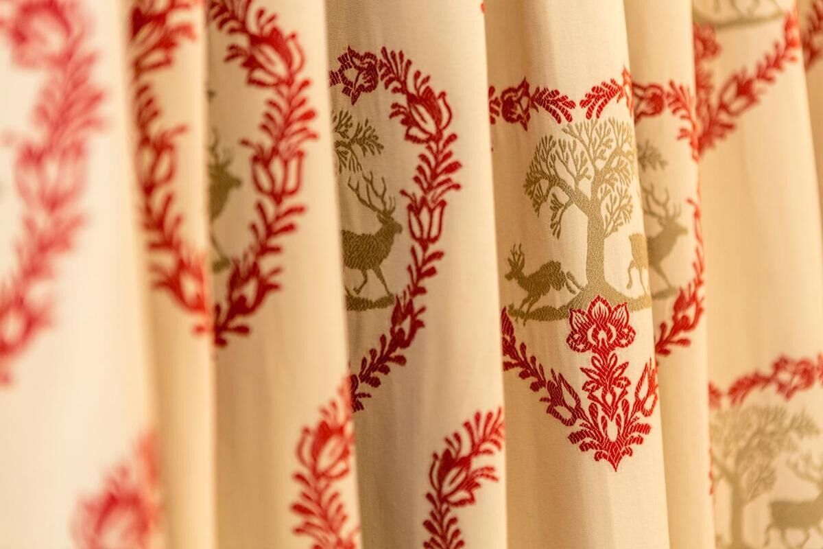 A close-up of a fabric with red and green embroidery featuring trees and deer.