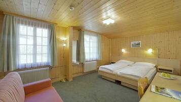 A wooden-paneled room with a double bed, a sofa, a table with a plate of apples, and a radiator.