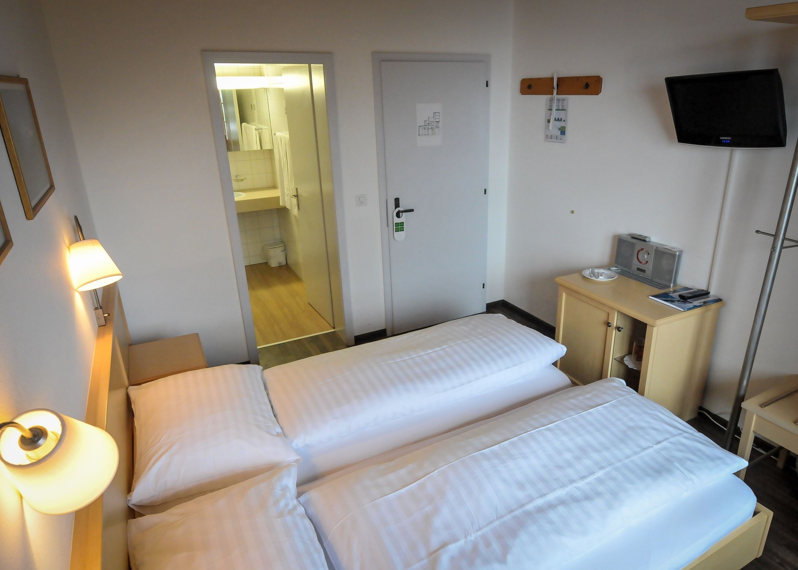 Ein Hotelzimmer mit zwei Betten, einem Schreibtisch, einem Computer, einem Fernseher und einer Lampe.