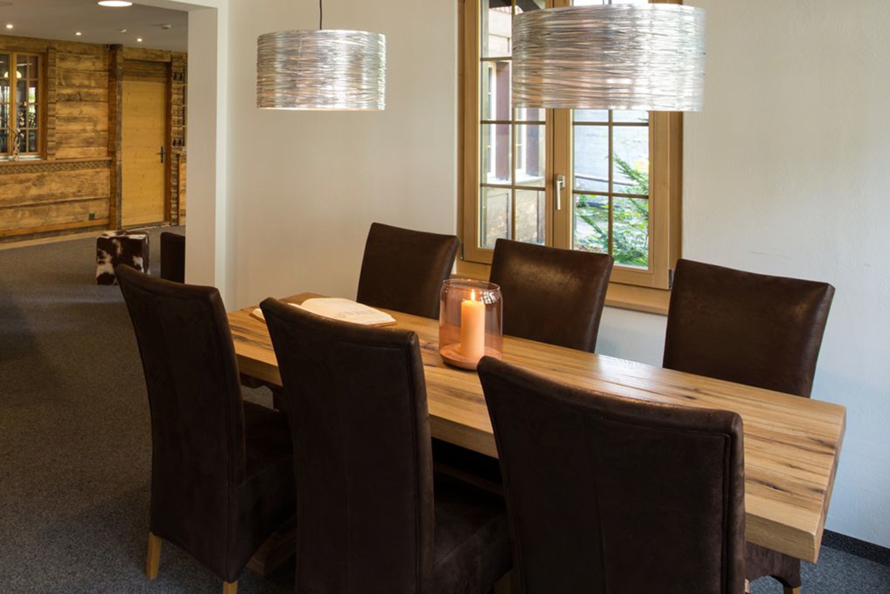 Un coin repas avec une table en bois et six chaises, une bougie et deux luminaires suspendus.