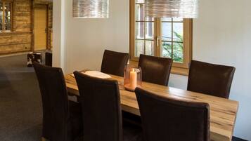 Un coin repas avec une table en bois et six chaises, une bougie et deux luminaires suspendus.