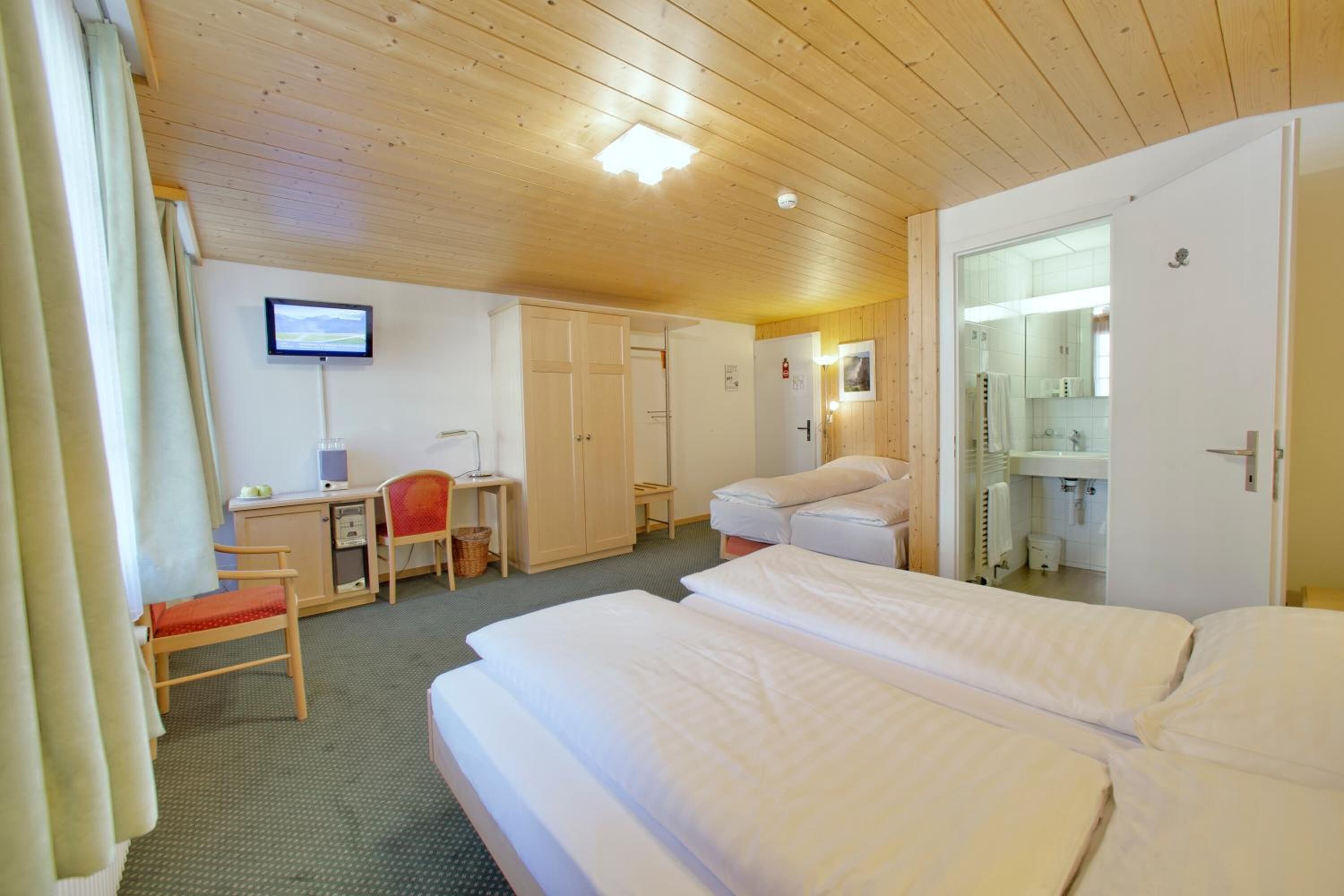 Ein Hotelzimmer mit zwei Betten, einem Schreibtisch mit Stuhl, einem Fernseher und einem durchgegangenes Badezimmer.