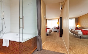 Ein Hotelzimmer mit Dusche, einem Bett mit roter Bettwäsche, einem Schreibtisch mit Lampe und Blick ins Freie.