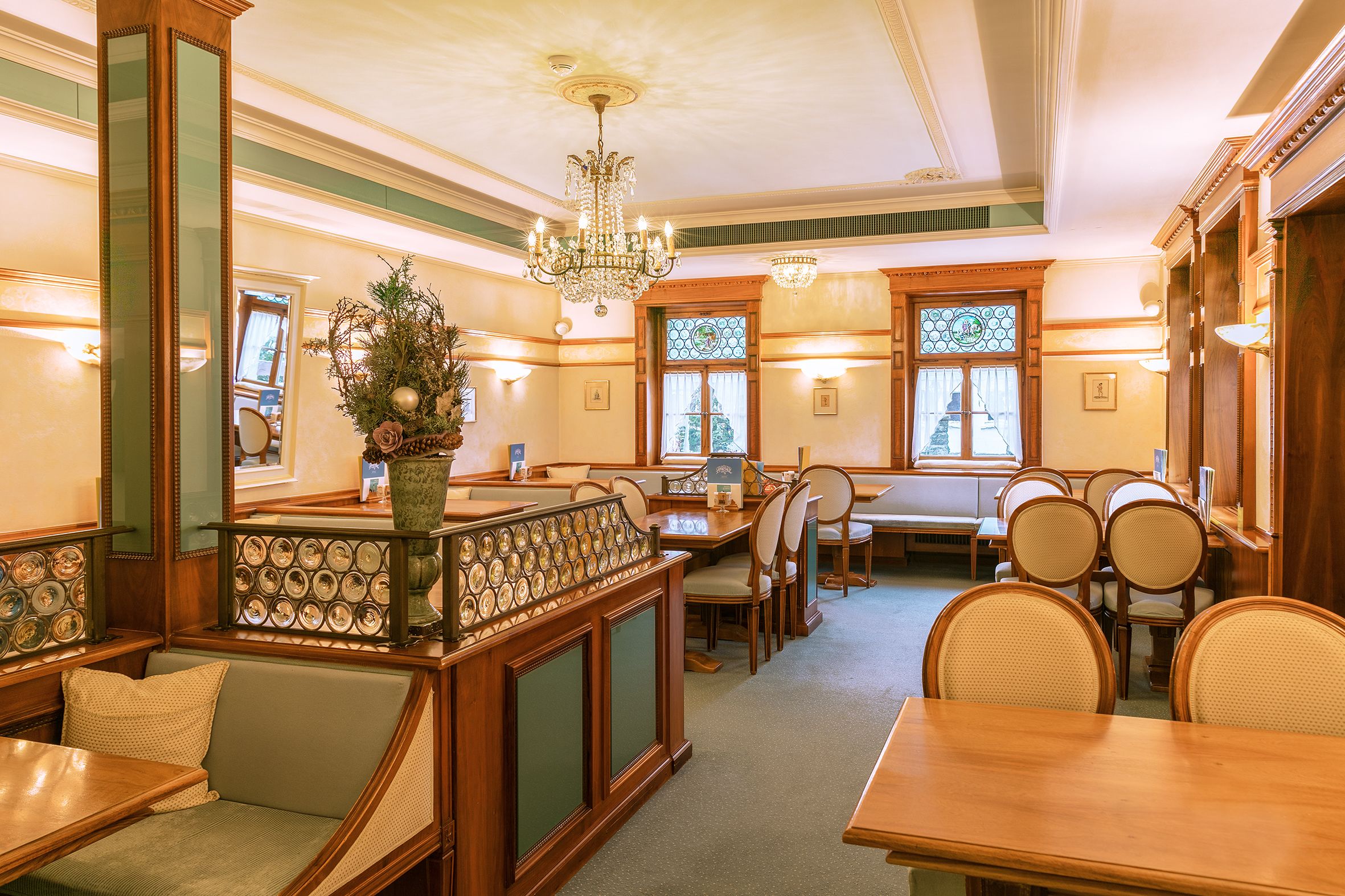 A dining area with wooden tables and chairs, a chandelier, and a decorative plant.