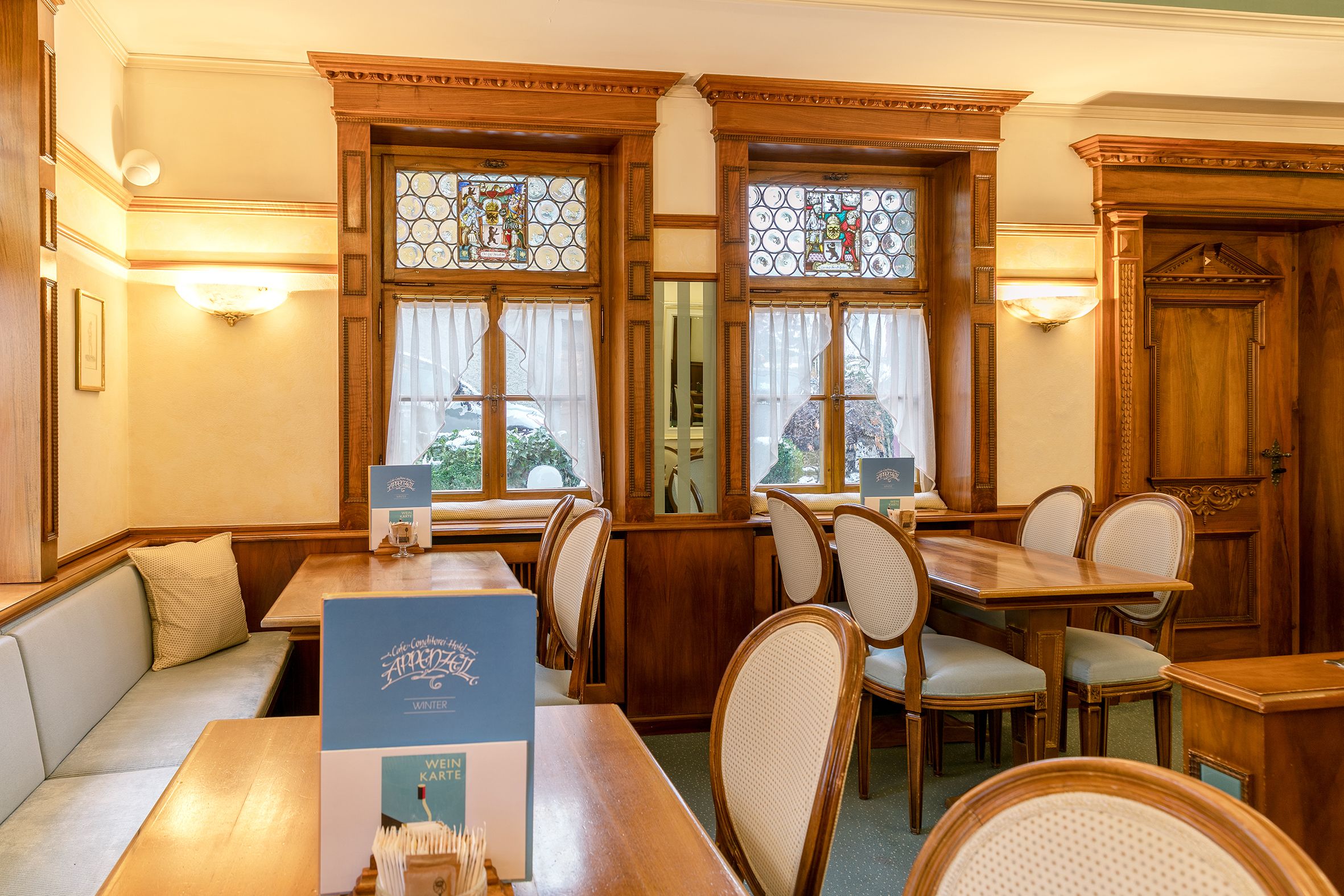 Een restaurantinterieur met houten meubels, glas-in-loodramen en een menukaart standaard.