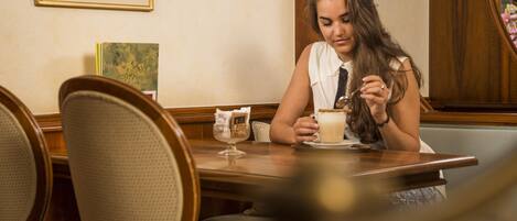 A woman sitting at a wooden table in a restaurant with a framed picture on the wall and a menu on the table.