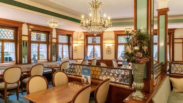 A restaurant with wooden tables and chairs, a chandelier, and a decorative vase with flowers.