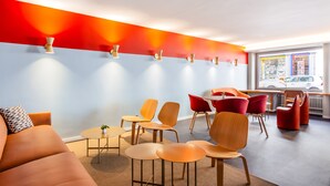 A modern waiting area with a mix of wooden and red chairs, a sofa, and a small table with a plant. - Hotel Marta - 1950’s architecture in Zurich’s vibrant old town, near main station (Zürich)