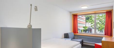 A modern hotel room with a bed, a desk, a chair, and a window with curtains.