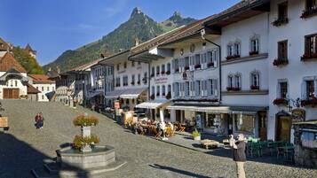 A historic town square with cobblestone streets, traditional buildings, and a mountain backdrop.