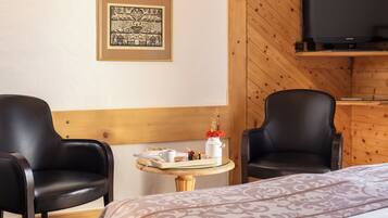 Ein Hotelzimmer mit zwei schwarzen Ledersesseln, einem kleinen runden Tisch mit Tablett, einem gerahmten Bild an der Wand und einem Fernseher auf einem Holzregal.