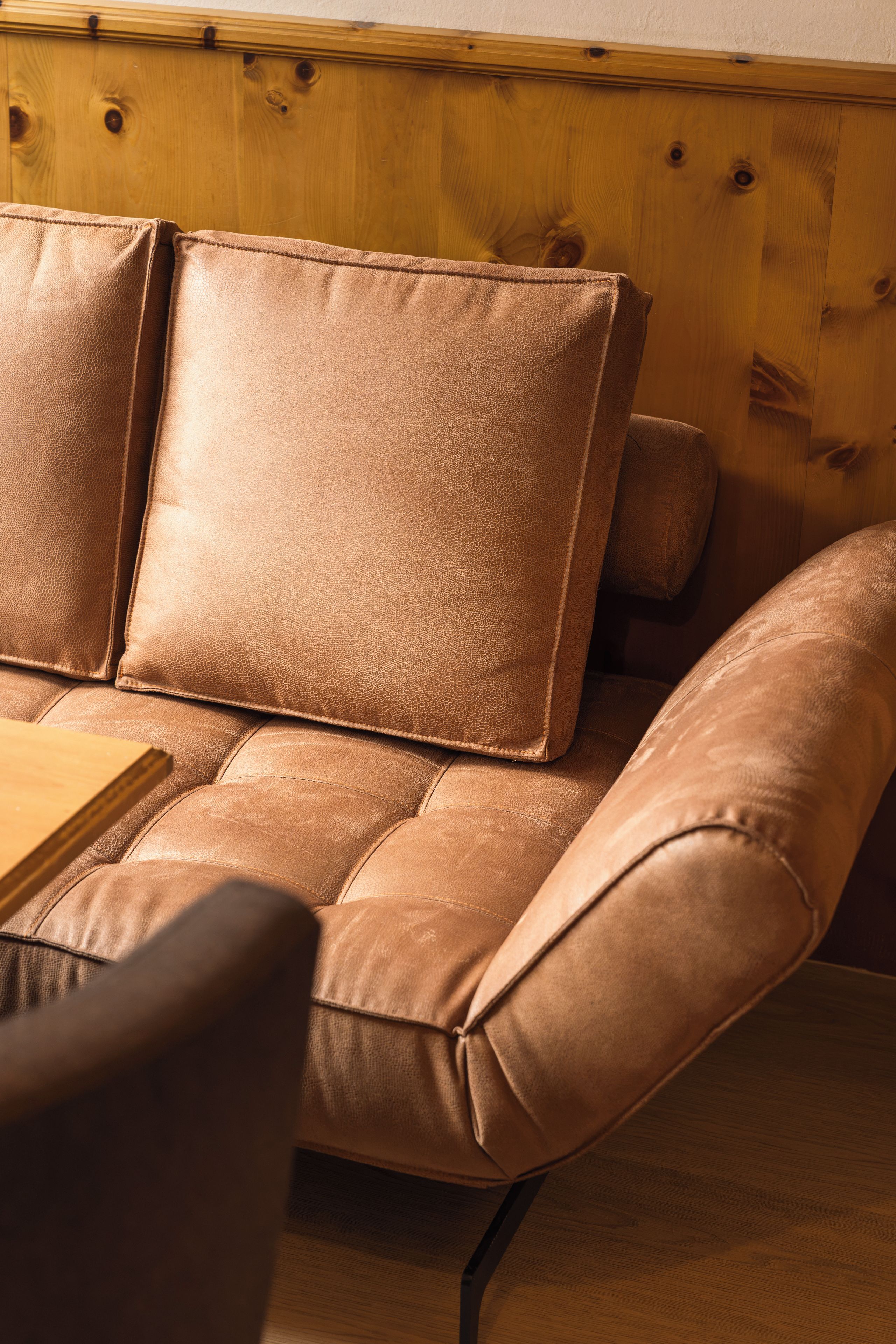 A brown leather sofa with a wooden headboard and a wooden table in front.