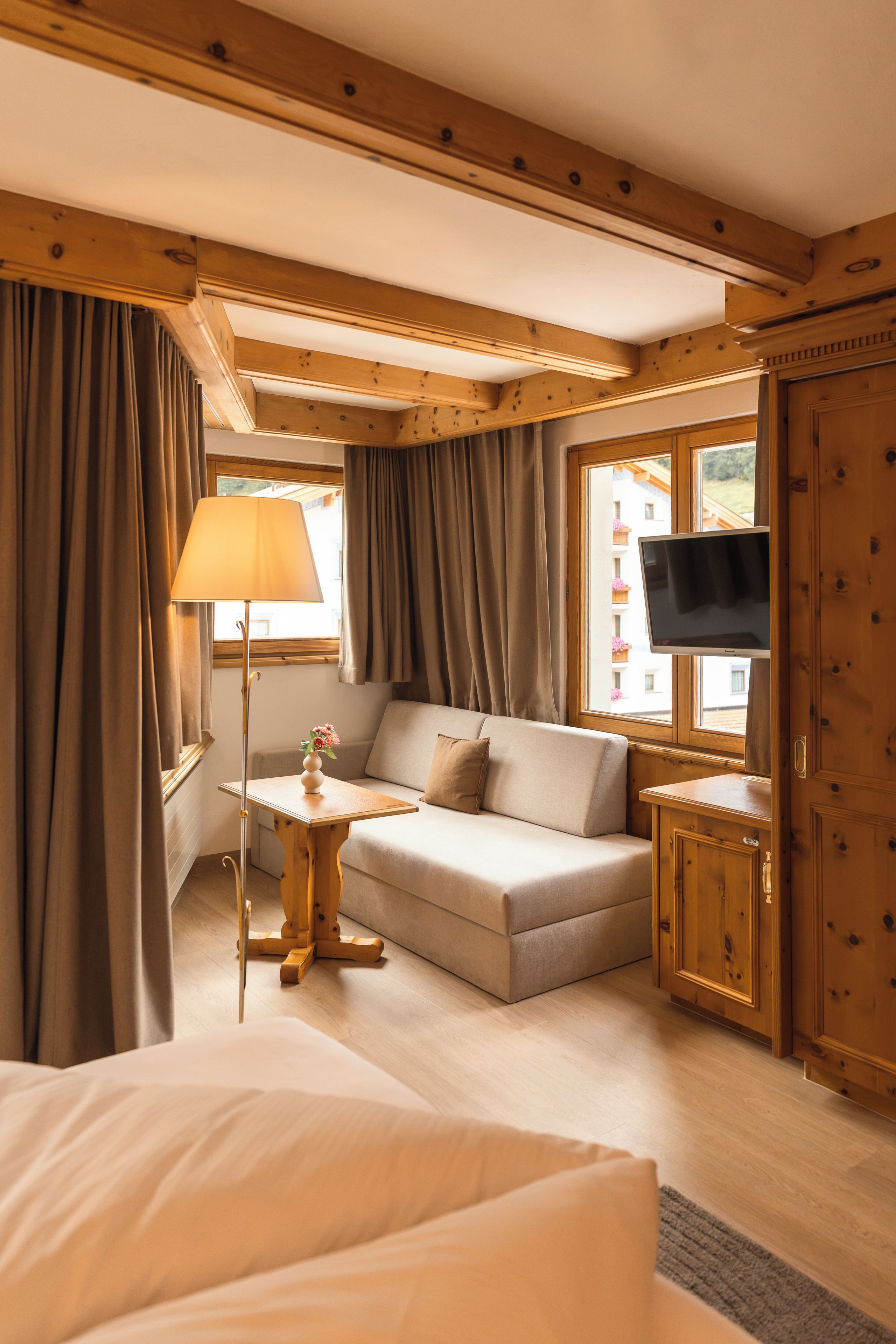 A hotel room with a bed, sofa, TV, and wooden walls.