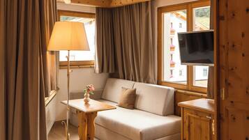 A hotel room with a bed, sofa, TV, and wooden walls.