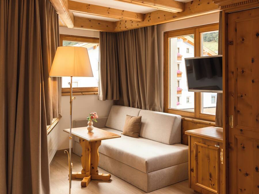 A hotel room with a bed, sofa, TV, and wooden walls.