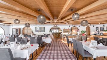 Un restaurante con vigas de madera en el techo, lámparas colgantes redondas y una alfombra escocesa que conduce a mesas cubiertas con manteles blancos y sillas.