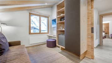 Ein moderner, hell eingerichteter Raum mit großem Fenster, Holzbalken, einer Couch, einem kleinen Tisch und einem violetten Pouf.