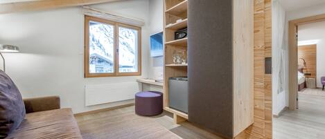 Una habitación moderna y luminosa con un ventanal grande, vigas de madera, un sofá, una mesita y un reposapiés morado.