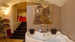 A bathroom with a large bathtub, a shower, and a painting of a woman. There are stairs leading to a red room in the background.