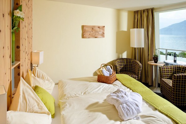 Une chambre d’hôtel avec un lit, deux chaises, une petite table, une fenêtre donnant sur la mer et une lampe fixée au mur.