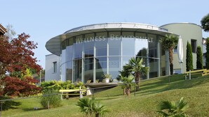 Un centre de bien-être moderne doté d’une façade en verre incurvée, d’un espace extérieur aménagé pour se détendre et d’un jardin paysager bien entretenu.