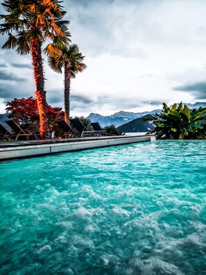 Une piscine à l’eau claire, entourée de chaises longues et de palmiers, avec des montagnes en arrière-plan.