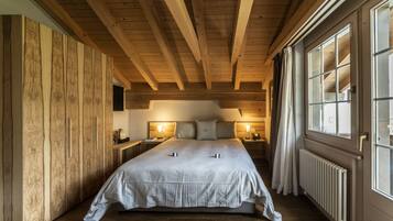 A cozy bedroom with a wooden ceiling, a large bed, bedside lamps, and a window with curtains.