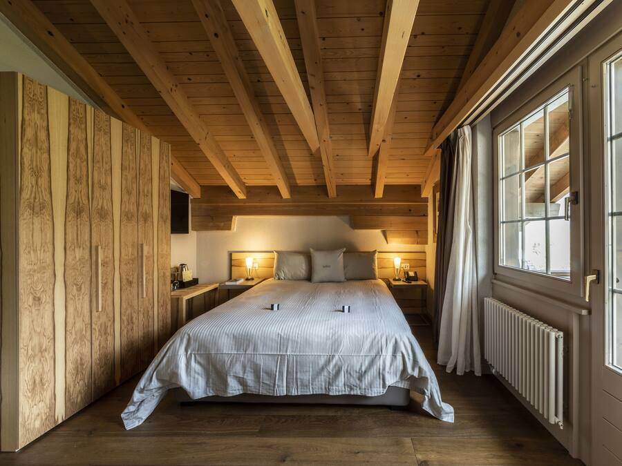 A cozy bedroom with a wooden ceiling, a large bed, bedside lamps, and a window with curtains.