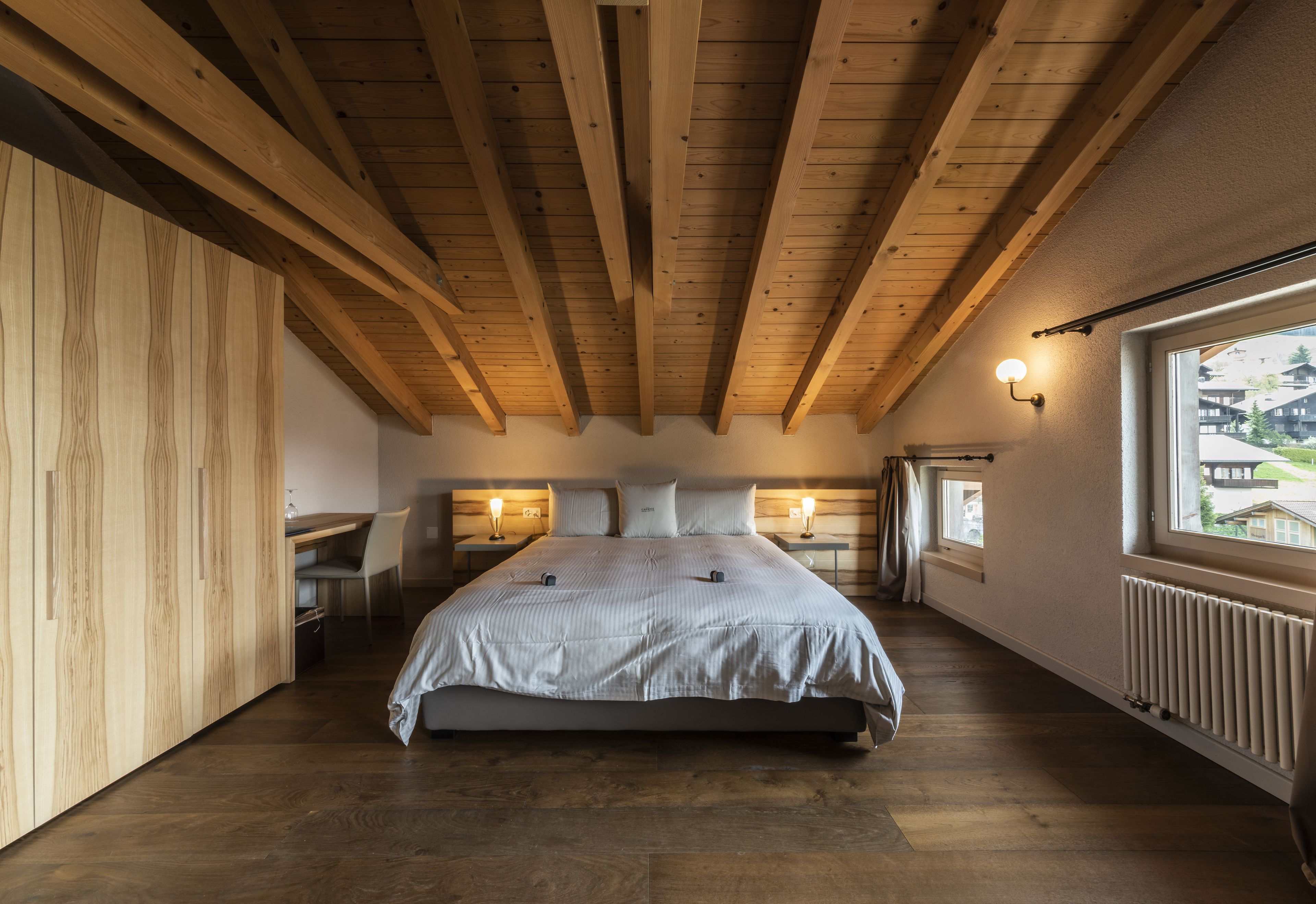 A bedroom with a wooden ceiling, a large bed, bedside tables, and a window with a view.