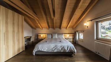 A bedroom with a wooden ceiling, a large bed, bedside tables, and a window with a view.