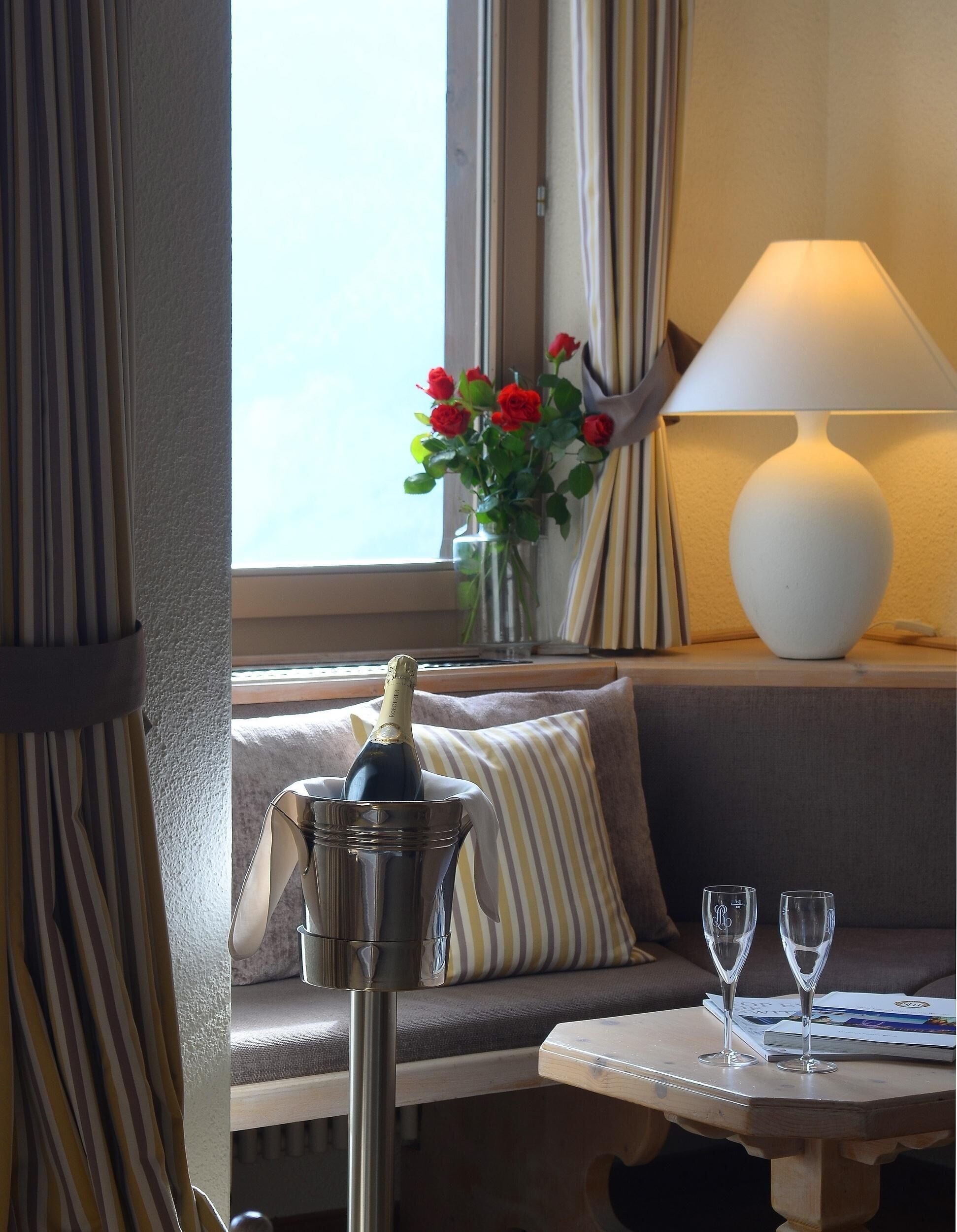 Habitación de hotel con sofá, una mesa con dos copas de vino, un florero con rosas rojas y una botella de champán en un cubo.