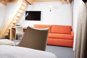 A modern room with a bed, a desk, a chair, an orange sofa, a TV, and a staircase.