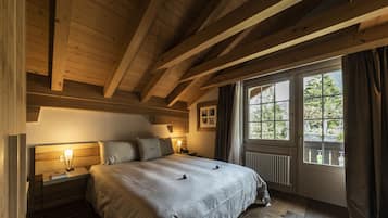 Une chambre avec un plafond en bois, une grande fenêtre avec des rideaux, un lit avec une tête de lit et une table de chevet avec une lampe.