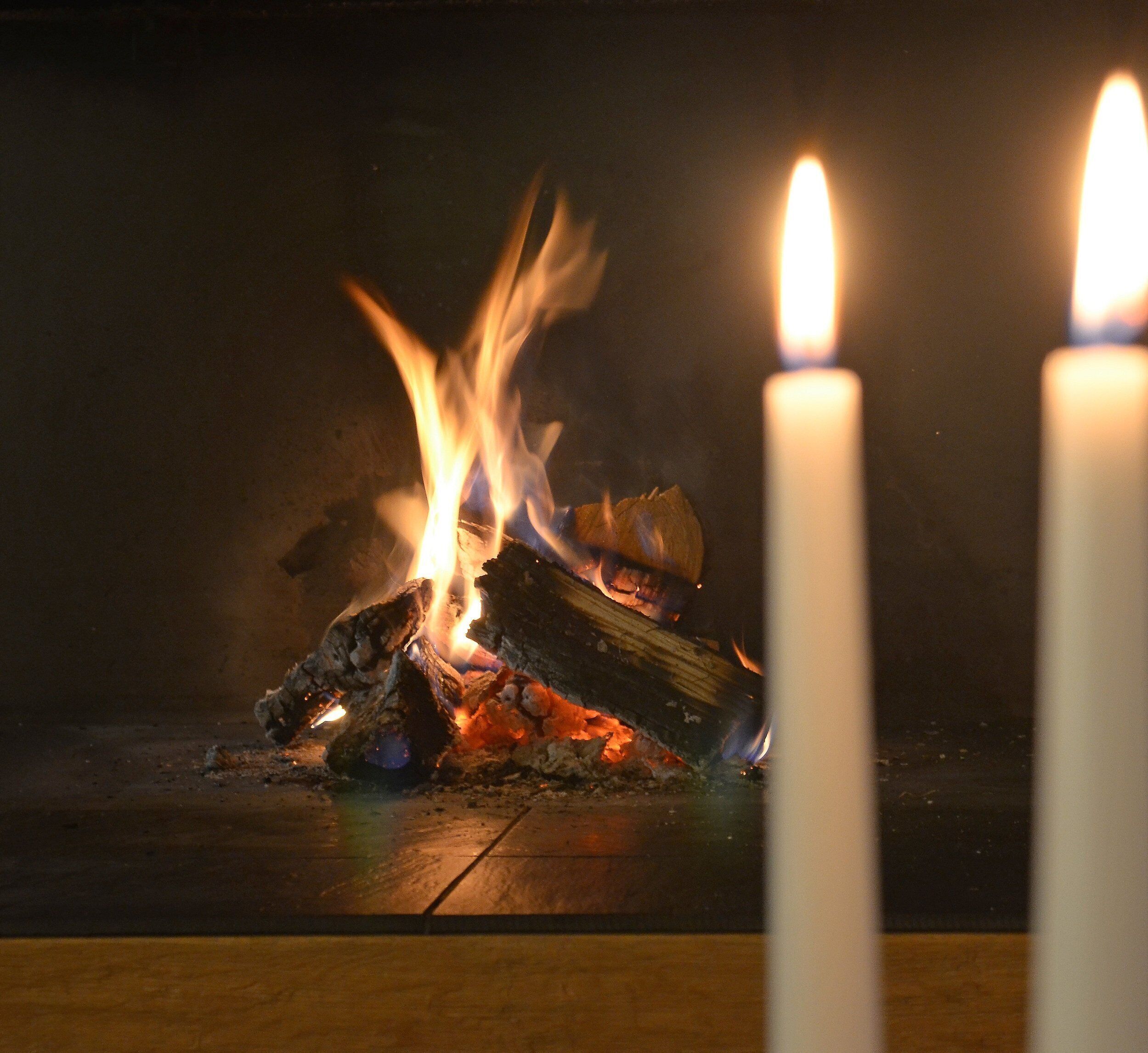 Ein Kamin mit brennenden Holzscheiten und zwei brennenden Kerzen.