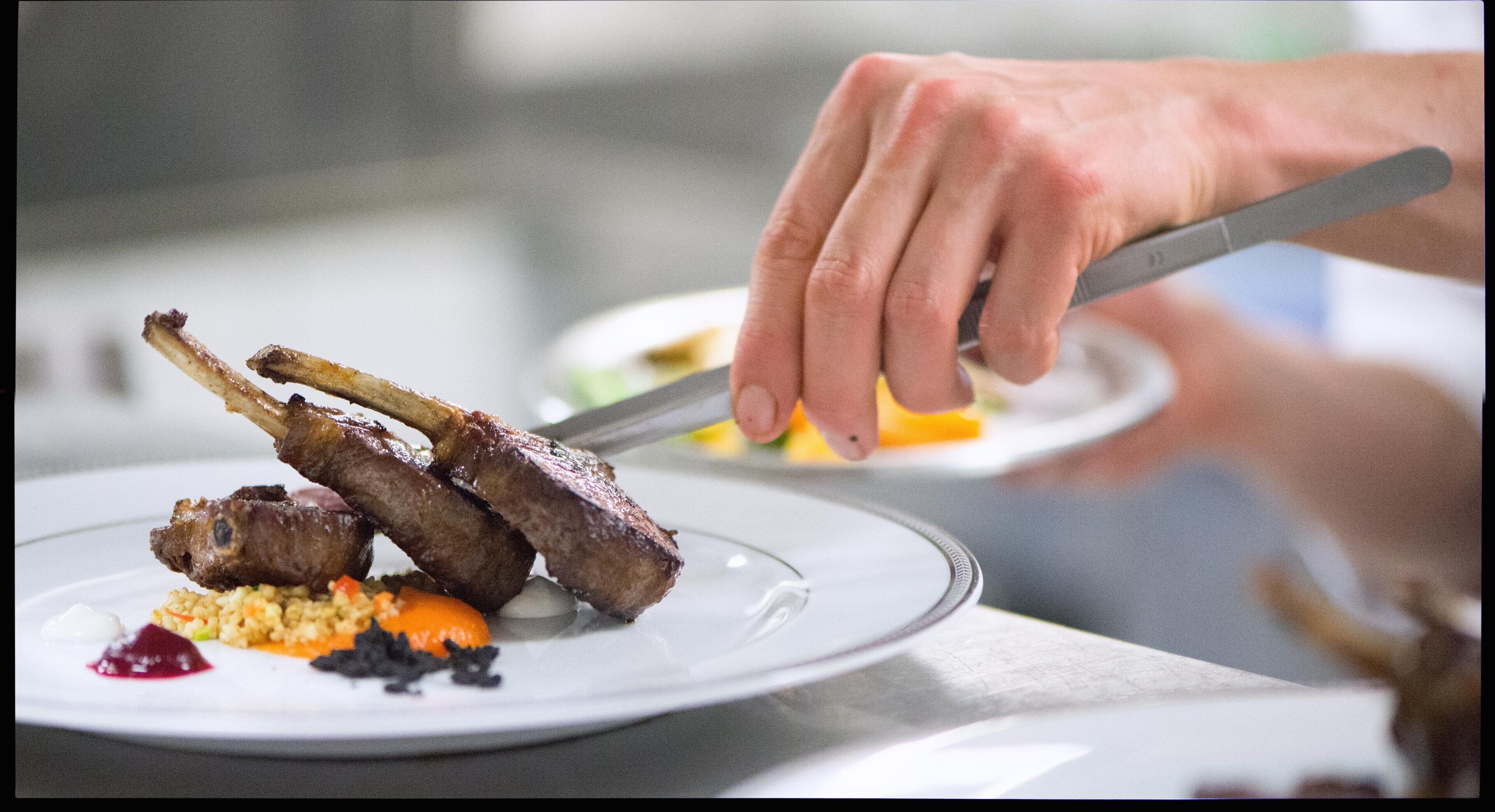 Una persona cortando un plato con chuletas de cordero y verduras.