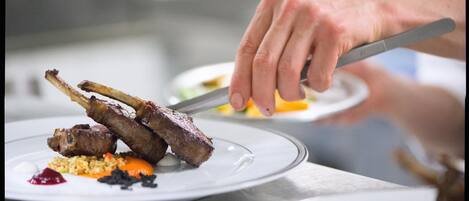 Una persona cortando un plato con chuletas de cordero y verduras.
