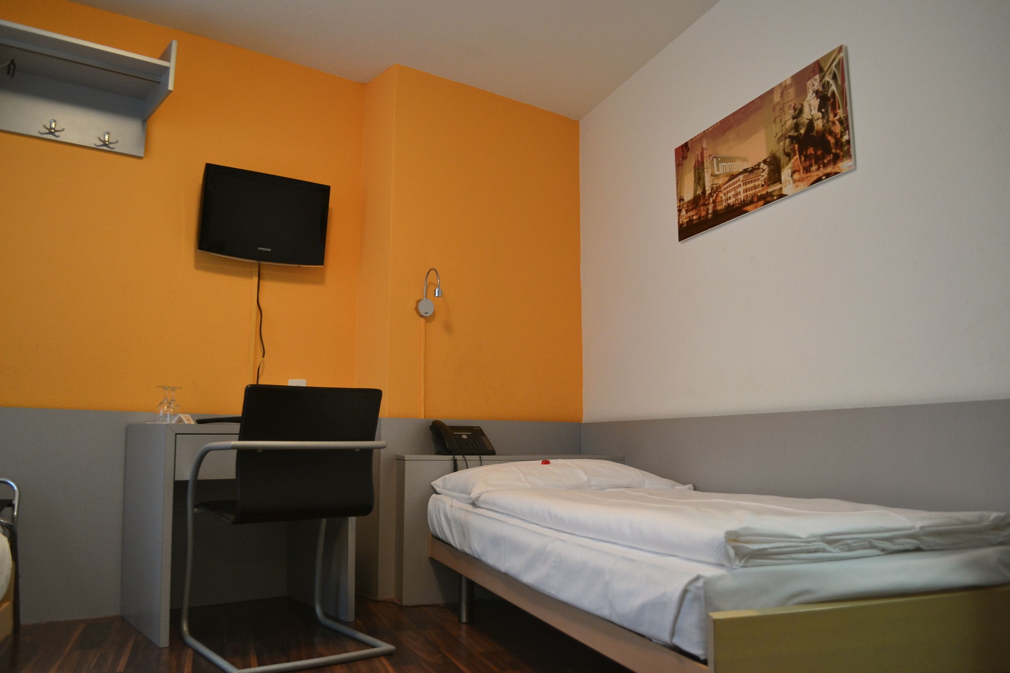 Ein Hotelzimmer mit einem Bett, einem Schreibtisch mit Stuhl, einem Fernseher und einem Bild an der Wand.