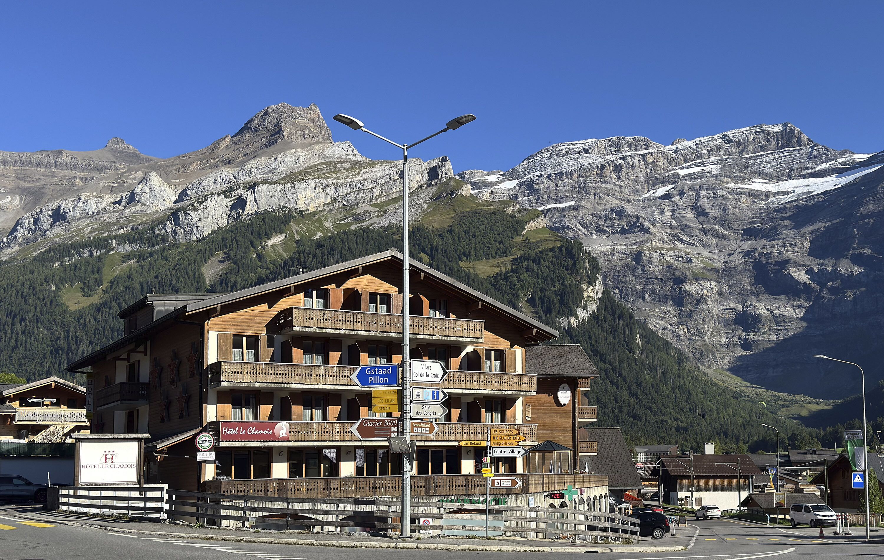 Un hôtel doté d’un balcon, avec une enseigne indiquant « Gstaad Pillion » et une autre indiquant « Hôtel Le Chamois ».