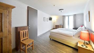 A hotel room with a bed, a desk, a chair, a desk lamp, and a TV.