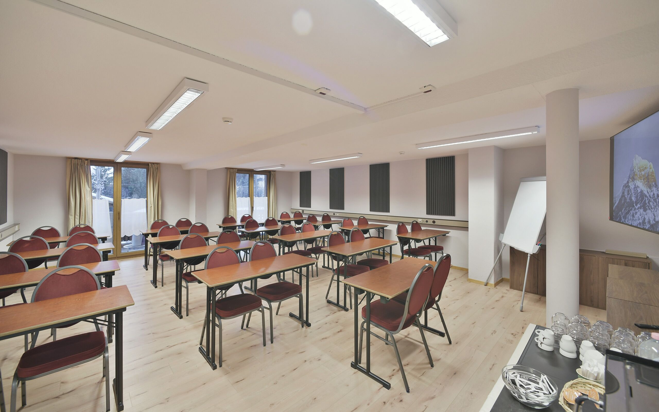 A conference room with rows of desks and chairs, a whiteboard, and a projector screen.