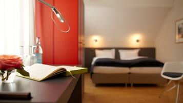 A modern bedroom with a bed, bedside lamps, a desk with a book and a vase of flowers.
