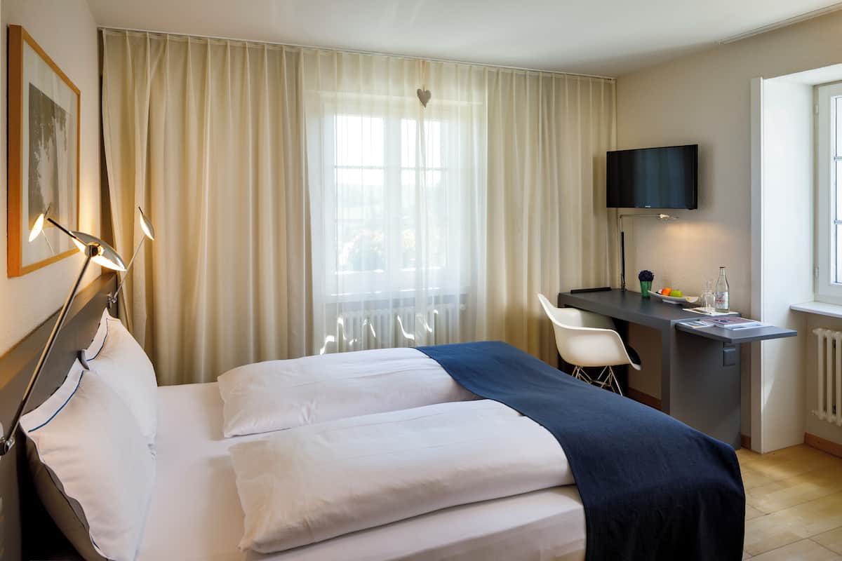 A hotel room with a bed, a desk, a chair, a TV, and a window with curtains.