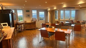 A spacious dining area with wooden tables and chairs, a buffet station, and large windows offering a view of the outdoors.