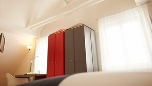 A hotel room with a bed, a desk, a chair, a wardrobe, and a window with curtains.