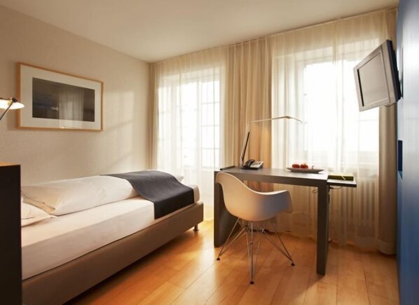 Une chambre d’hôtel moderne équipée d’un lit, d’un bureau, d’une chaise et d’un téléviseur fixé au mur.