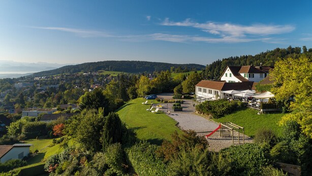 A hillside property with a large house, a swimming pool, and a red-roofed deck.